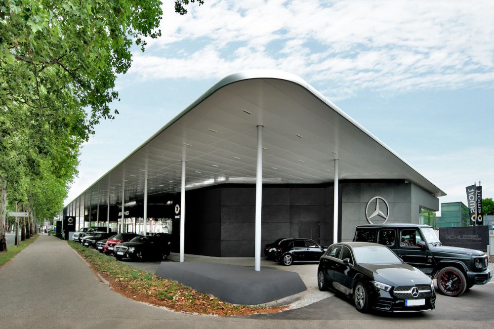 Mercedes-Benz Autohaus mit Autos, blauem Himmer, grüner Baumreihe
