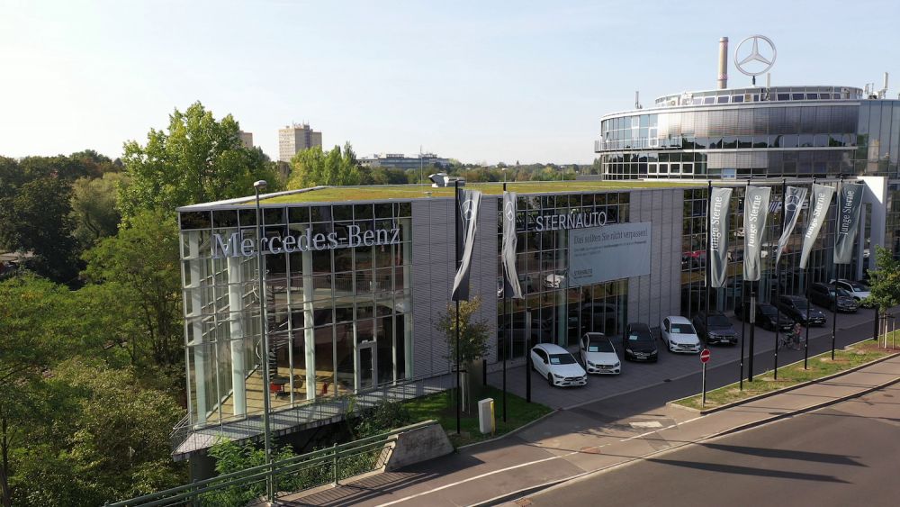 Erhöhte Ansicht von der Glasfassade und das Mercedes-Benz Logo vom Autohaus STERN Auto Leipzig mit viel Grün drumherum