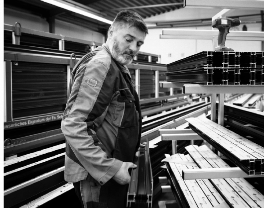Schwarz Weiss Bilder vom Mitarbeiter in der Werkstatt, der ein ein Aluminium-Fensterprofil trägt