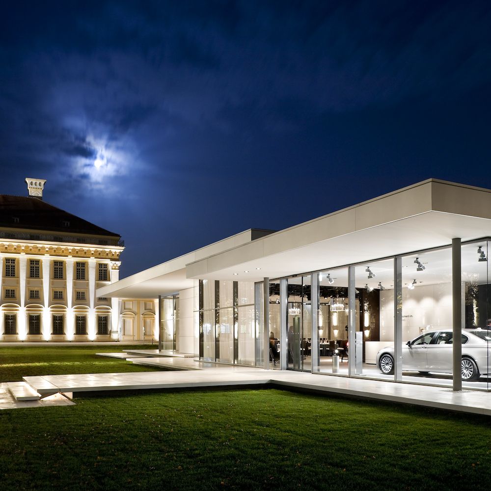 Beleuchteter BMW Kubus Pavillon mit Glasfassade abends