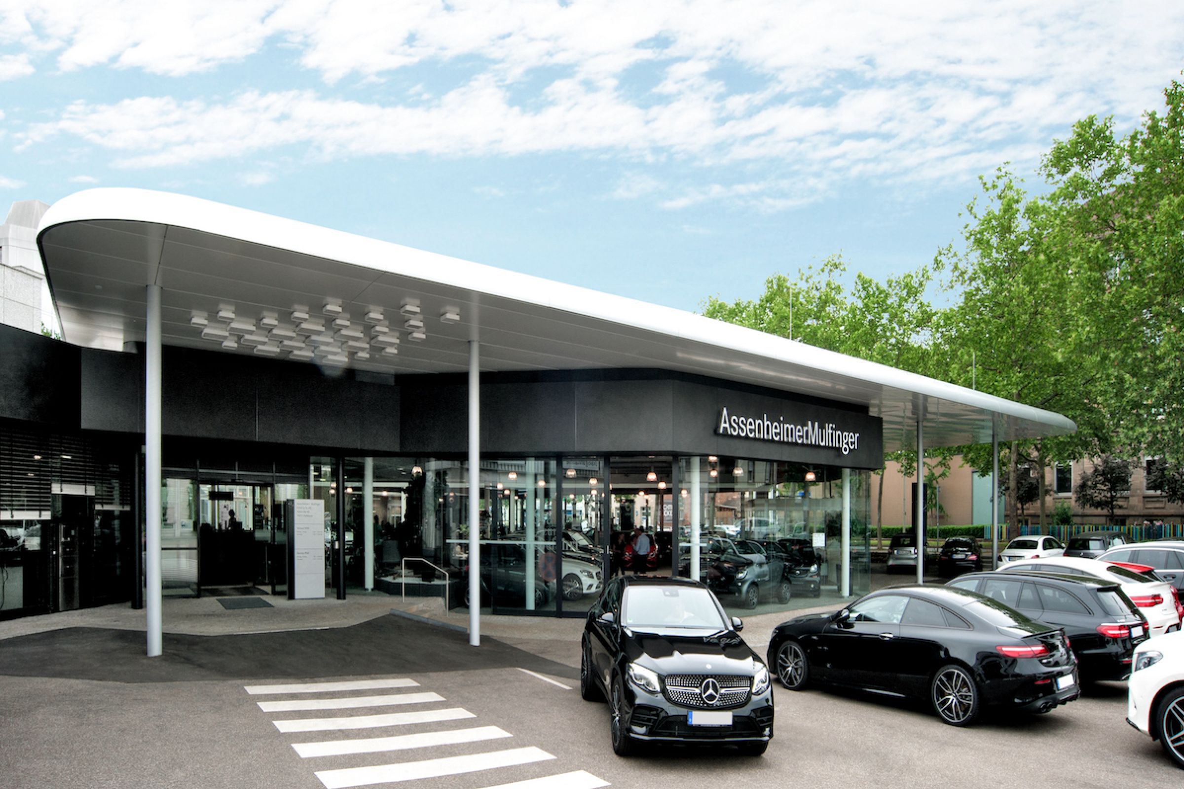Eingang von Mercedes-Benz Autohaus mit geparkten Autos und Verglasung